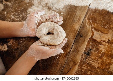 Child making dough for bread, shaping into a bagel on a wooden table surface. Shallow depth of field. - Powered by Shutterstock