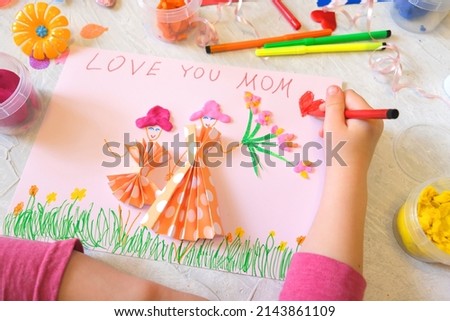 Child making homemade greeting card from paper and clay, plasticine as gift for Mothers day, Birthday or Valentines day . Arts  crafts concept.