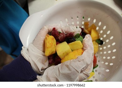 Child Making Smoothie Hands With Gloves Holding Frozen Fruit Pineapple Raspberries Blueberries And Spinach  Over A White Plastic Colander Strainer 