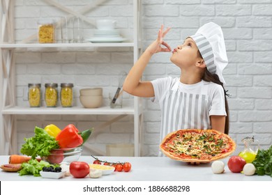 child making tasty delicious gesture by kissing fingers. little girl in chef hat and an apron cooking pizza in the kitchen.