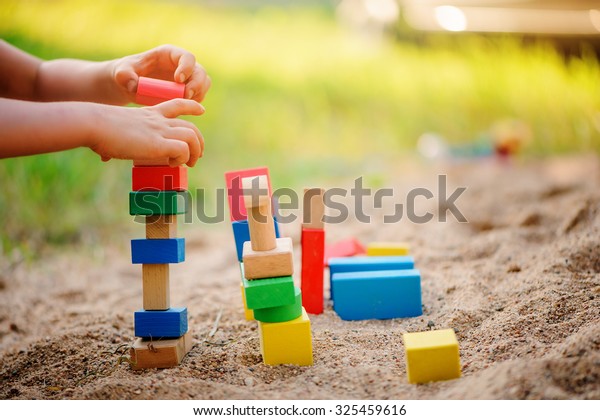 child\
making toy house from wooden bricks in\
sandbox