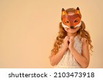 A child in a masquerade carnival mask of a fox, hand-made from glitter foamiran. Little cute cheerful comical girl in the role of a fox. The child is preparing for the carnival, holidays. 