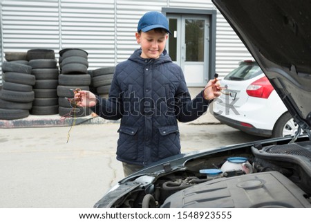 A child mechanic is standing with wires at a broken car.