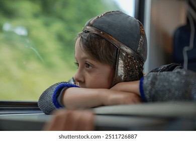 Child in medieval armor, resting on a table by the train window, lost in thought while looking outside. Wearing a helmet and chainmail, immersed in a moment of quiet reflection - Powered by Shutterstock