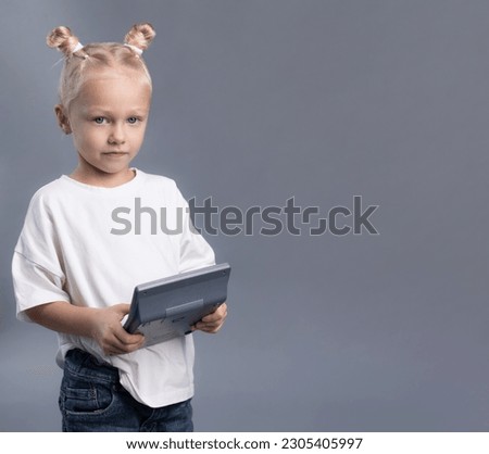 Child with messy buns in white T-short looking at camera on grey background. Little girl holding calculator 