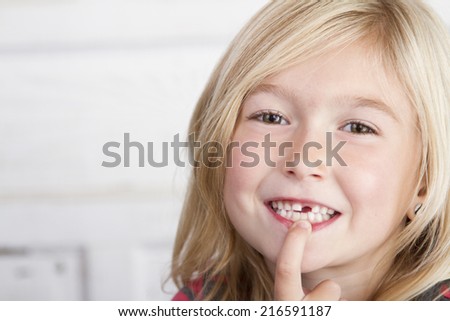 Child missing front tooth pointing at it with her finger
