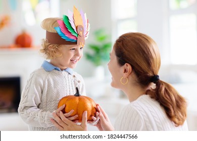 Child and mother celebrate Thanksgiving. Kid holding pumpkin in paper turkey hat. Autumn fun crafts and art. Mom and little boy in decorated living room. Warm knitted wear. Fall season decoration.