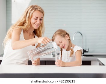 Child With Mother Drinking Water From Glass. Happy Family At Home In Kitchen 