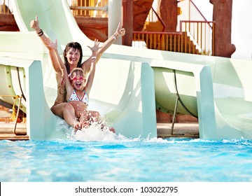 Child with mother on water slide at aquapark. Summer holiday.