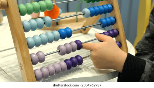Child moves beads on abacus learning to count in kindergarten closeup. Little kid plays with tool improving motor skills and logical thinking development