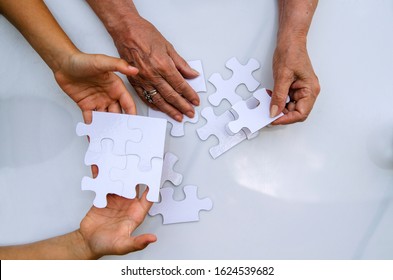 Child And Old Woman Hands Connecting Puzzle White Pieces.Above View On Jigsaw Parts In Senior And Young Female Hands.Playing And Friendship In Pension  