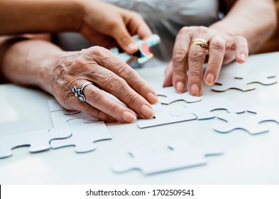 Child And Old Woman Hands Connecting Puzzle White Pieces. Jigsaw Parts In Senior And Young Female Hands.Playing And Bonding In Self Isolation Quarantine