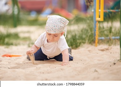 Child On All Fours. Hand Pours Sand On The Children's Sandbox.