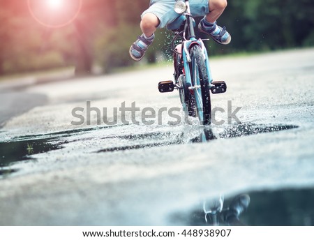 child on a bicycle at asphalt road in summer. Bike in the park moving through puddle on rainy day