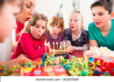 Child on birthday party blowing candles on cake being helped by friends and the mother