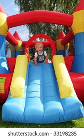 Child On Bouncy Castle. Inflatable Blow-up Toy For Kid In Garden