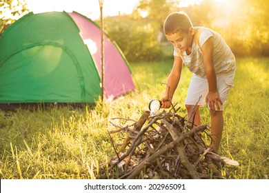 Child On A Camping Trip Using A Magnifying Glass To Light A Fire