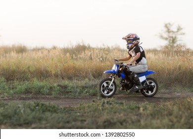 Child On His Small Motorcycle. Small Biker Dressed In A Protective Suit And Helmet. The Kid Is Engaged In Motocross.