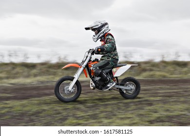 Child On His Small Motorcycle. Small Biker Dressed In A Protective Suit And Helmet. The Kid Is Engaged In Motocross.