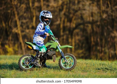 Child On His Small Motorcycle. Small Biker Dressed In A Protective Suit And Helmet. The Kid Is Engaged In Motocross.