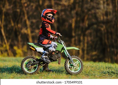 Child On His Small Motorcycle. Small Biker Dressed In A Protective Suit And Helmet. The Kid Is Engaged In Motocross.