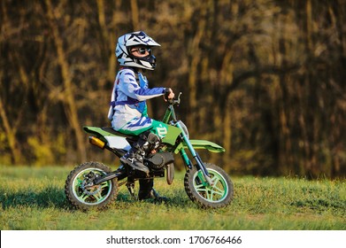 Child On His Small Motorcycle. Small Biker Dressed In A Protective Suit And Helmet. The Kid Is Engaged In Motocross.