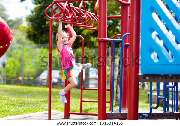 Child on\
monkey bars. Kid at school playground. Little girl hanging on gym\
activity center of preschool play ground. Healthy outdoor activity\
for kids. Sport for young\
children.