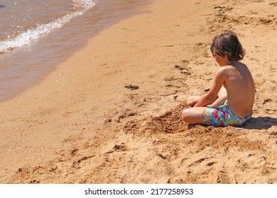 A Child On The Sand Of A Beach, Sitting, Meditating, Or Playing Alone