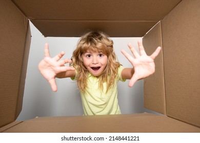 Child Opens Carton Box And Pulling Out Gift From It. Small Boy Looking In Parcel Box And Happy To Receiving A Surprise. Young Kid Showing Joy On His Face. Unpacking Cardboard Box For Kids.