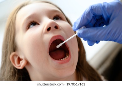 Child Opens Mouth For COVID Or Monkeypox PCR Test, Doctor Holds Swab For Saliva Sample From Student. Nurse Hand And Little Kid Face Close-up. Concept Of Corona And Smallpox Virus Testing In School.