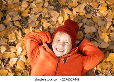 Child In An Orange Jacket Lies On The Fallen Leaves In The Autumn Forest. Rest In The Fall In Nature.