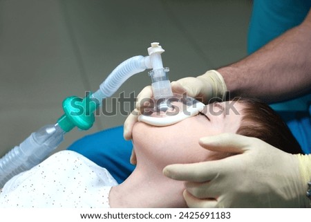 A child with an oxygen mask on his face. Preparing the child for anesthesia. Dental treatment under general anesthesia. Dental surgery under general anesthesia. Surgical intervention. Side view.