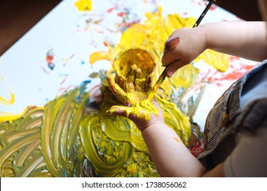 Child Painting Her Hand With Yellow Paint And Paintbrush. Finger Painting Or Art Therapy For Children. Fun Activities For Toddlers. 