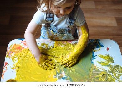 Child Painting With Her Hands On The Table At Home Using Yellow Paint. Finger Painting Or Art Therapy For Children. Fun Activities For Toddlers. 