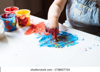 Child Painting With Her Hands On The Table At Home Using Blue And Red Paint. Finger Painting Or Art Therapy For Children. Fun Activities For Toddlers. Close Up. 
