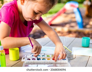 Child Painting On Paper Outdoors On Picnic Table. Painting Outside During The Fall. Girl Working On Art Project.