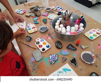 Child Painting Rocks On A Table With Colored Paints