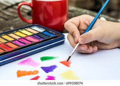 Child Painting With Watercolor Paints On A White Paper Book In Natural Light