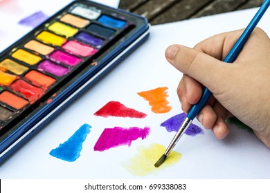 Child Painting With Watercolor Paints On A White Paper Book In Natural Light