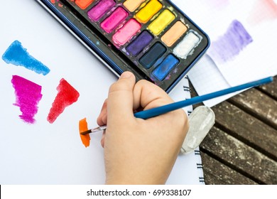 Child Painting With Watercolor Paints On A White Paper Book In Natural Light