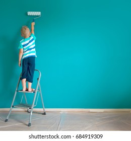 The Child Paints The Blue Wall With A Roller. The Boy Holds A Large Brush For Painting. Home Repairs.