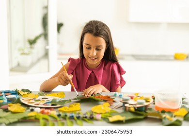 A child paints a picture of an autumn leaf with paints. Children's hands. Favorite hobby, materials for creativity.