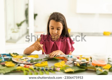 A child paints a picture of an autumn leaf with paints. Children's hands. Favorite hobby, materials for creativity.