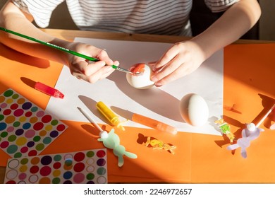 Child paints white egg. Creativity with children. girl's hands with eggs on the background of a table with paints, brushes, eggs, holiday flags.do-it-yourself. Handicrafts and crafts for Easter. DIY - Shutterstock ID 2246972657