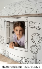 A child and a paper playhouse. Paper house for drawing. Children's toys. The girl is playing.