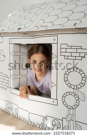 A child and a paper playhouse. Paper house for drawing. Children's toys. The girl is playing.