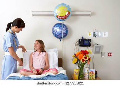 Child Patient Sitting In Hospital Bed With Nurse And Get Well Soon Balloons And Cards