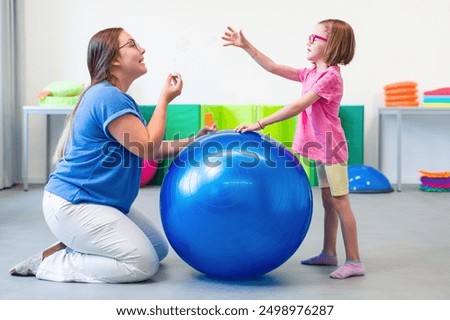 Child with physical disability in bilateral coordination physiotherapy. Child living with cerebral palsy exercising with her therapist during physiotherapy.