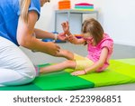 Child with physical disability in physical therapy session. Child living with cerebral palsy exercising with her therapist during physiotherapy.