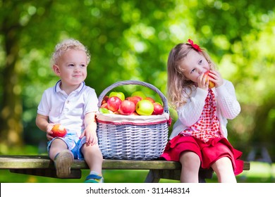 Child Picking Apples On A Farm In Autumn. Little Girl And Boy Playing In Apple Tree Orchard. Kids Pick Fruit In A Basket. Toddler Eating Fruits At Harvest. Outdoor Fun For Children. Healthy Nutrition.